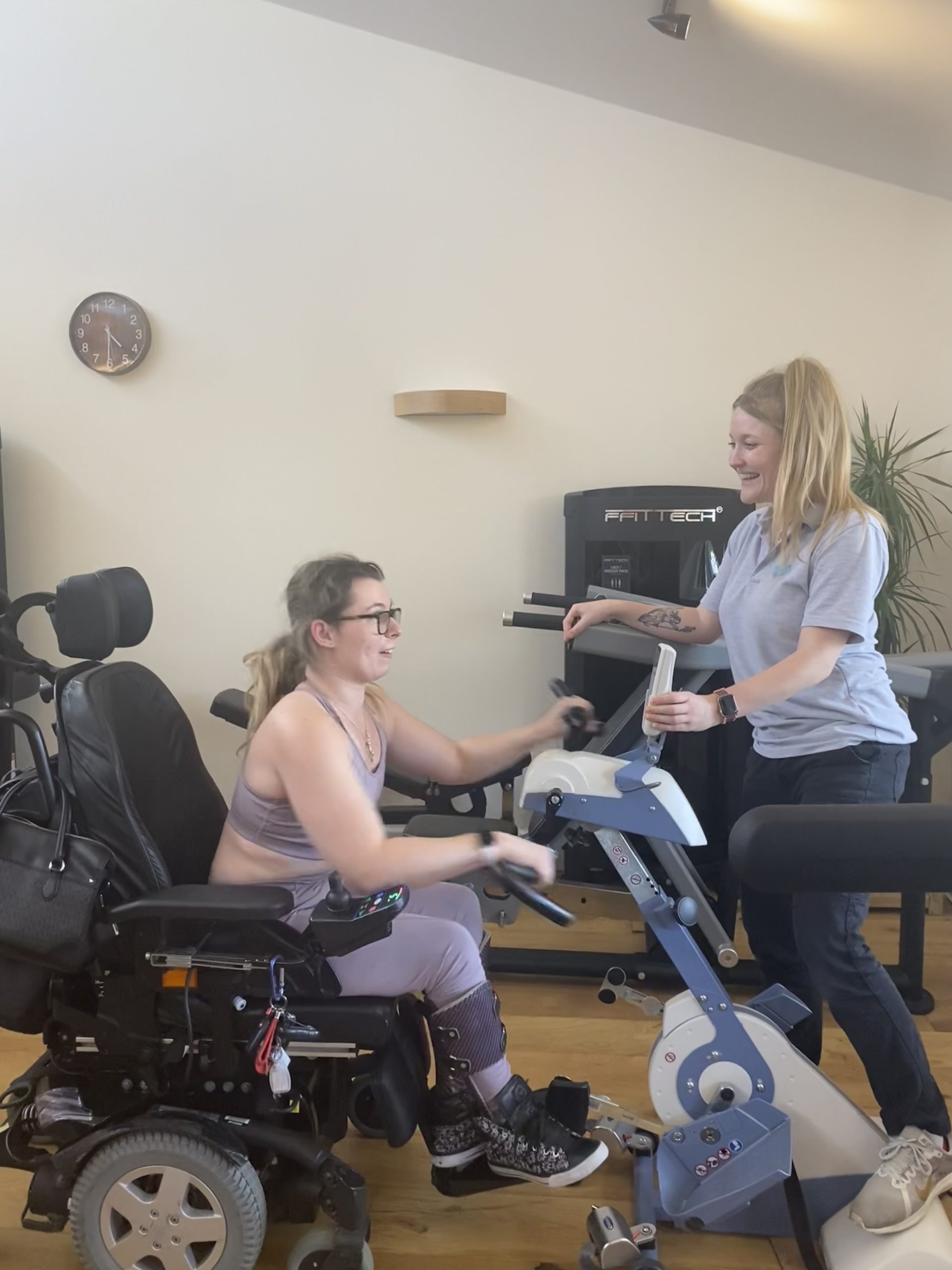 marissa is using lower limb rehab device the motor med. physio sophie is stood in front of her smiling