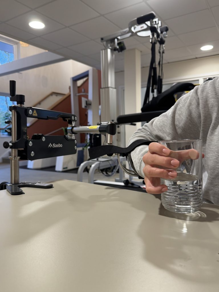 hand holding glasss whilst arm is supported by the saebo mas mini