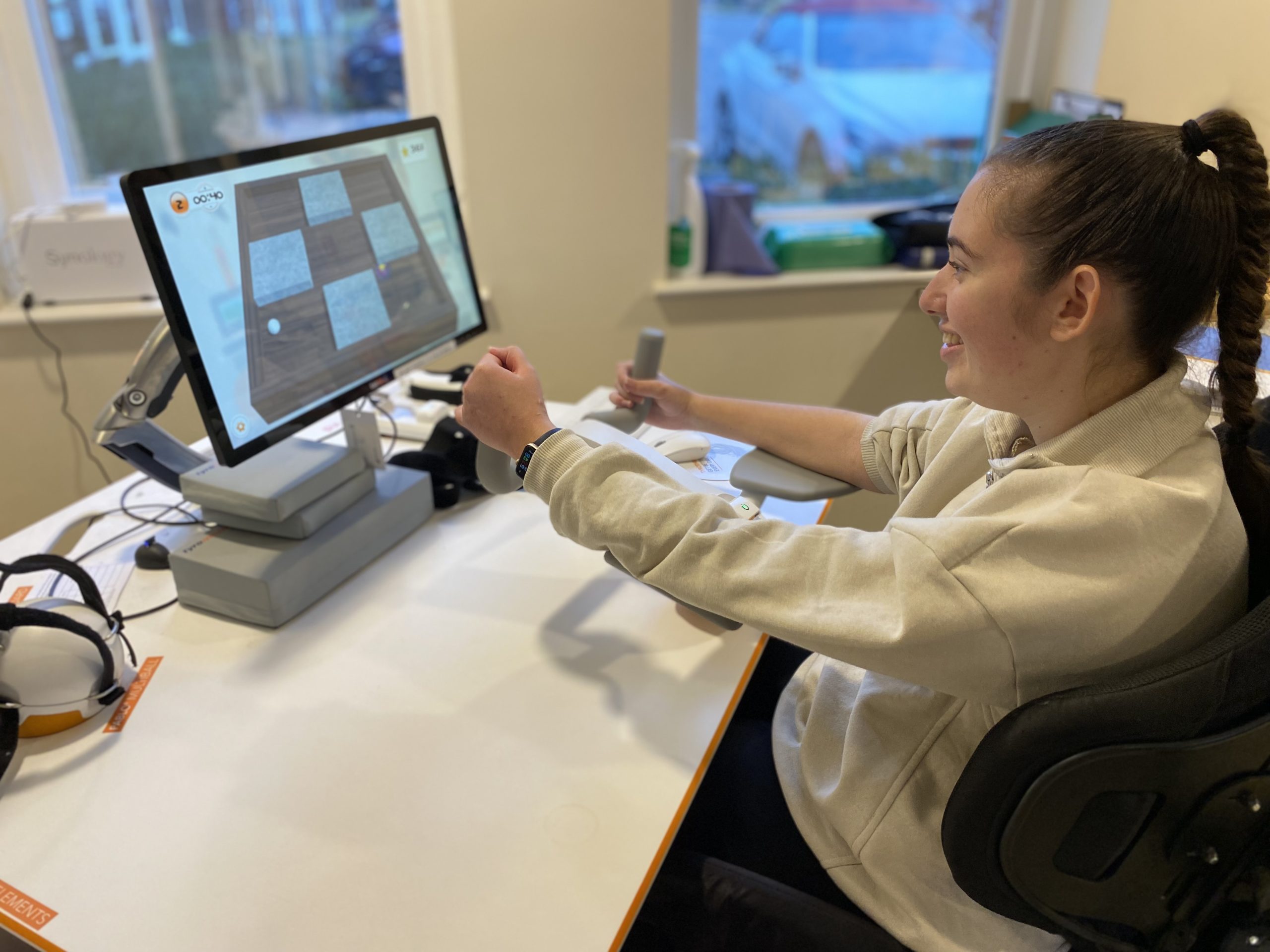 Macy is using a joy stick to operate the VR game on screen to improve upper body rehabilitation