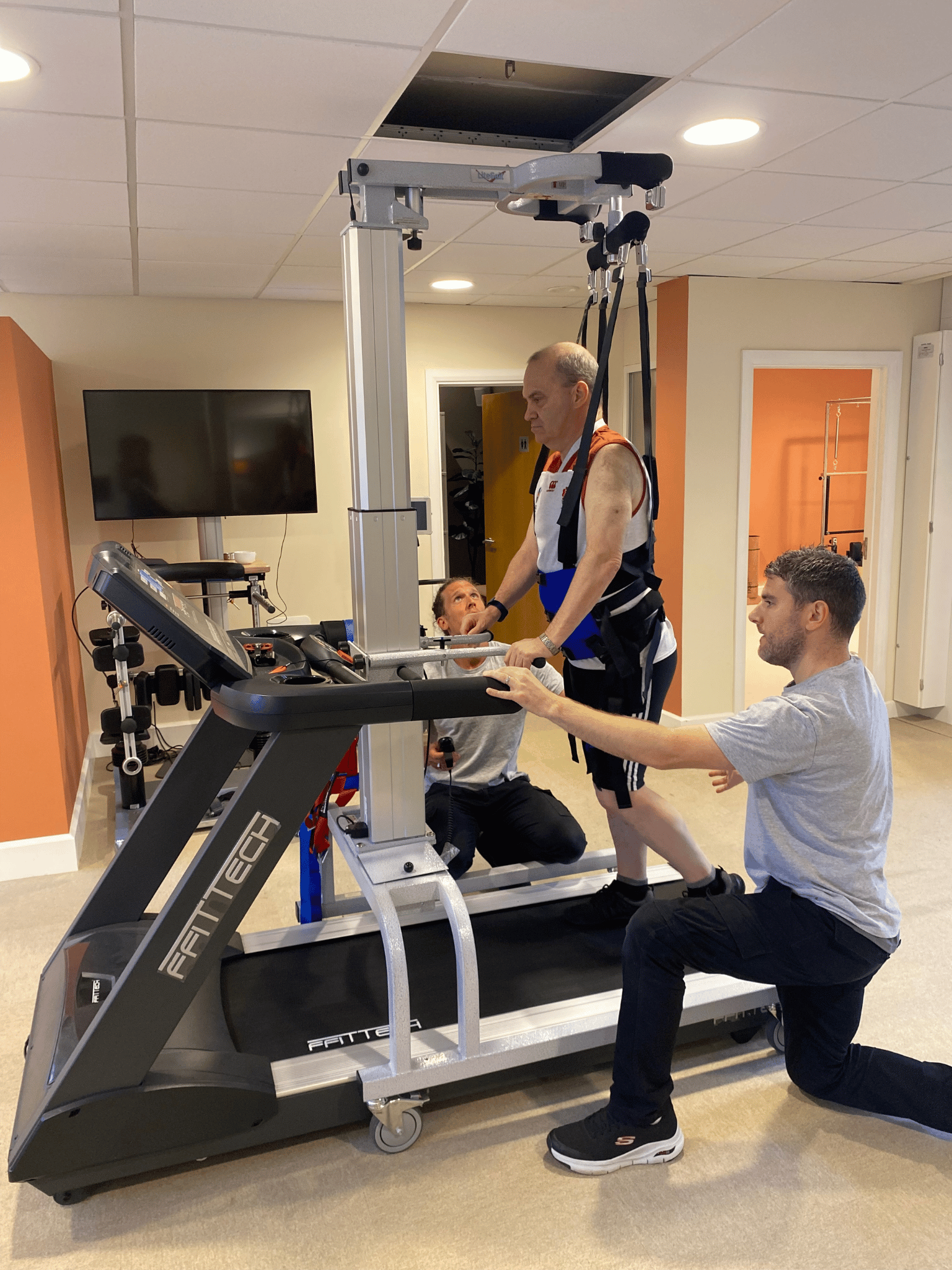 Side view of Stephen strapped into the LiteGait Harness whilst using treadmill to help improve his Gait. Phsyios tom and tom are either side of him.