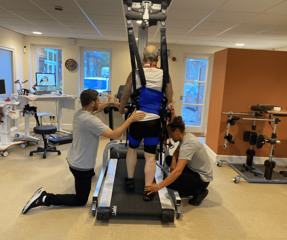Stephen is strapped into the LiteGait harness whilst using the treadmill. Physios tom and tom are either side of him supporting his leg and waist as he moves.