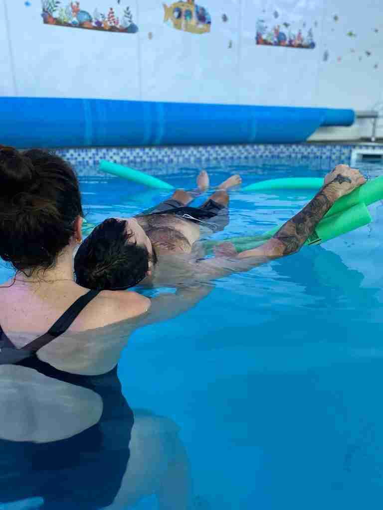 Physio Bex supports Elliot by his neck and shoulders whilst he floats on his back in the hydro pool