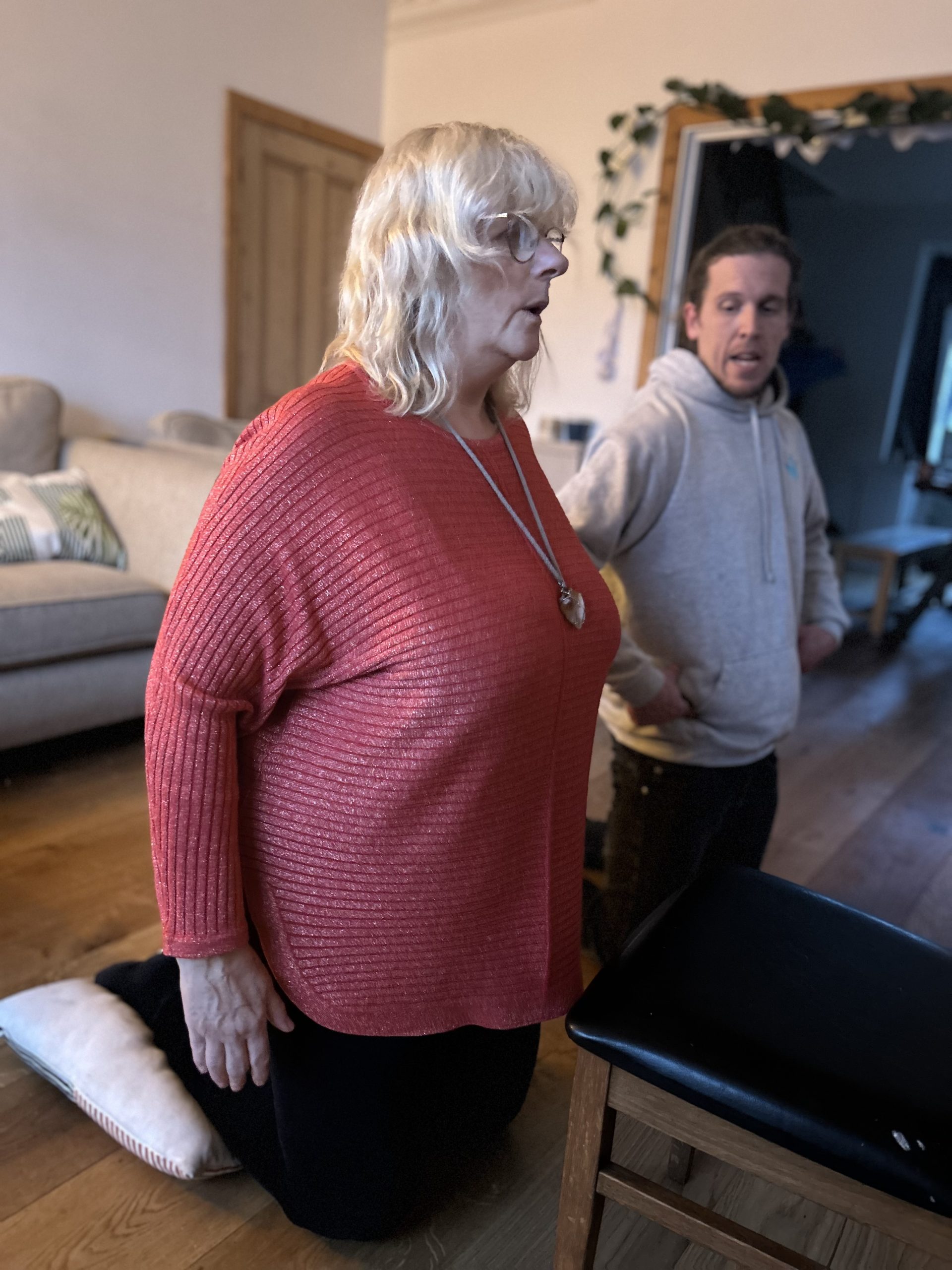 Community Physiotherapist Tom and Julie are knelt on the floor kneel next to each other whilst Julie completes rehabilitation exercises at home.