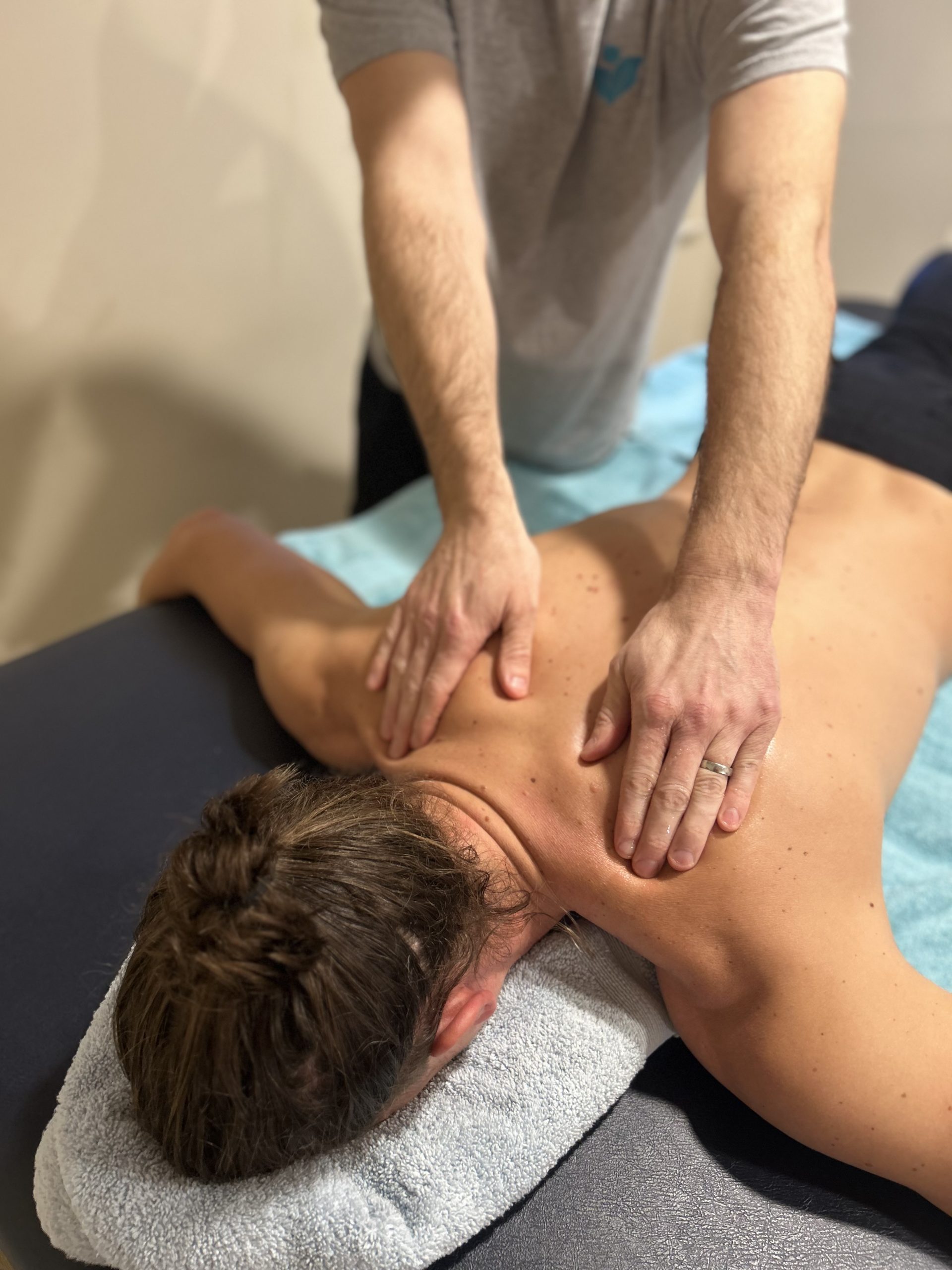 tow hands massage the shoilders of a man face down on a massage bed
