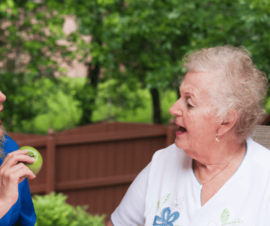 older lady is sat next to a therapist who is off screen she is doing some speech exercises